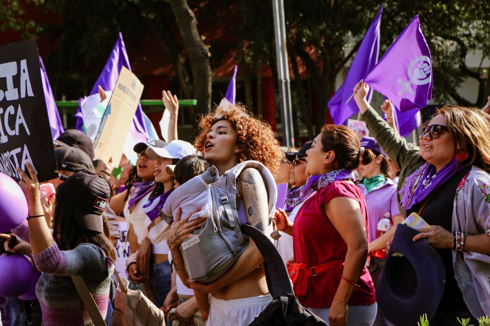 Women marching together with purple flags, a young mother leading chants while carrying her child